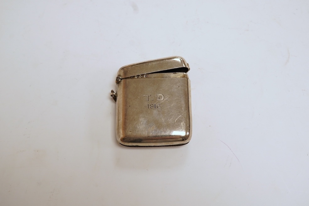 A George V silver mounted rectangular cigarette box, with later engraved inscription, Birmingham, 1932, 13.7cm, together with a similar silver vesta case and two modern silver wine labels. Condition - poor to fair